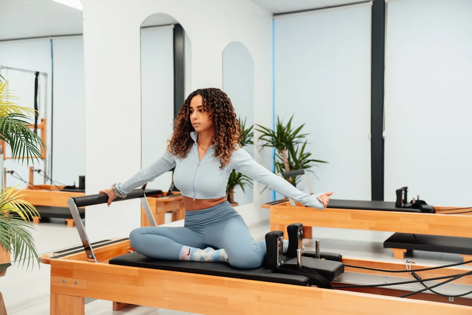 A woman sitting on a reformer, twisting with one arm out