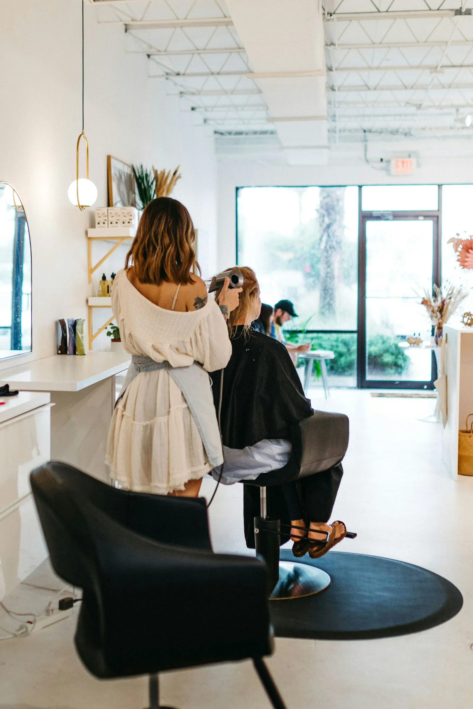 A stylist at work on a client in a bright salon, one chair, plants by the window